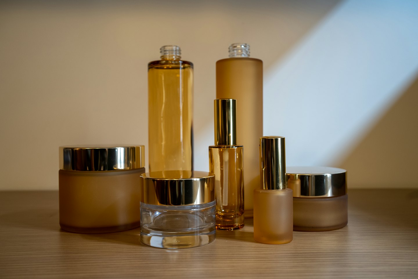 Various cosmetic bottles and jars with gold lids on wood.